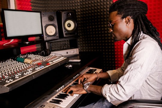 African man with dreadlocks playing synthesizer in recording studio