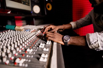 African musician with dreadlocks adjusts the sound on the mixing console in the recording studio...