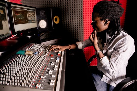 African musician with dreadlocks creates sound on the mixing console in the recording studio close-up