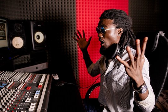 African musician with dreadlocks looks at the computer sitting in the recording studio