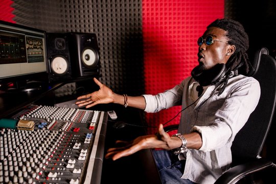 Surprised African musician with dreadlocks with outstretched arms in the recording studio