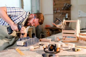 Bearded carpenter with safety glasses drills wooden bar
