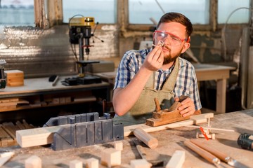 Bearded carpenter whittling a wooden block holding wooden sawdust