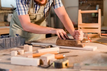 Bearded carpenter planing a wooden bar