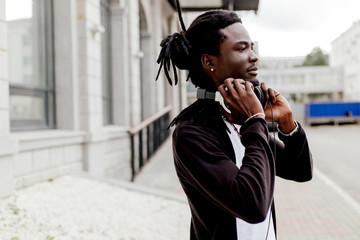 African man with dreadlocks standing in the middle of the city wearing full-size headphones on his head