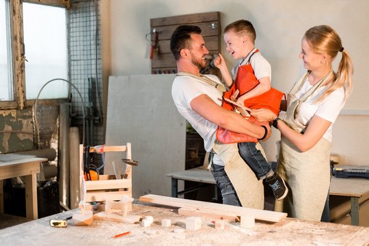 Happy family standing in carpentry workshop hugging each other. Dad took his son in his arms standing next to mom