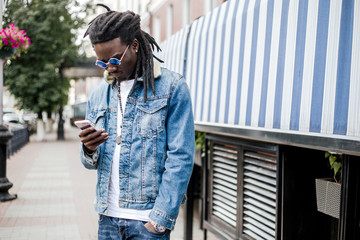 African man in denim jacket with sunglasses standing on the street looking at the phone screen