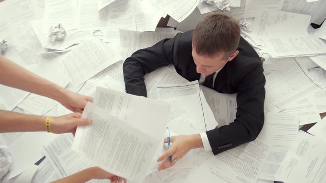 An office employee can not cope with the number of documents. A young tired person sits in a pile of papers, sorts out a lot of documents and does not have time on time.