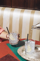 A girl holds a glass of gin and tonic while tonic water is poured, into an elegant pop-colored bar