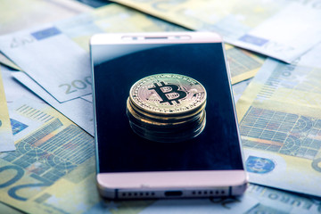 Bitcoin coin on the phone screen on the background of the Euro banknotes. Blockchain and the future of cryptocurrency