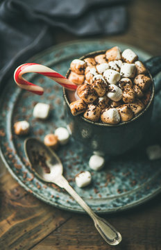 Winter warming sweet drink hot chocolate with marshmallows and cocoa in mug with Christmas holiday candy cane on wooden background, selective focus