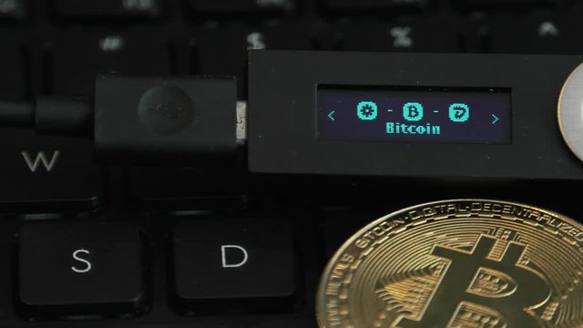 Cold hardware wallet for crypto. Connected to a computer to store Bitcoin, Litecoin and other cryptocurrencies.Notebook, Laptop keys in the background. Vires in numeris. Strobe effect on display.