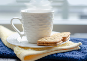 A cup of hot coffee in white cup with steaming and biscuit