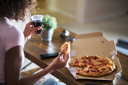 Woman Eating Pizza And Drinking Cola While Sitting On Sofa Watching Tv In Home Late At Night