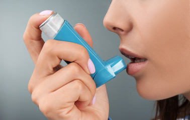 Young woman using asthma inhaler on color background, closeup