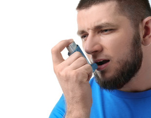 Young man using asthma inhaler on white background