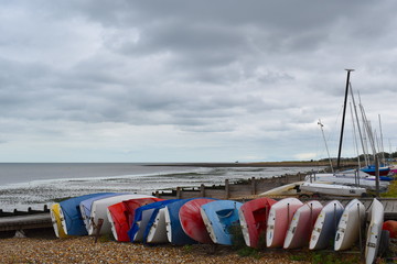 Small sailing boats lined up near the sea on the pebbles at Whitstable. Whitstable, Kent, UK