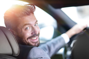 rear view, young man driving his car, looking at camera