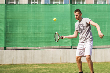 young man beginner tennis player doing sports on the court on summer day