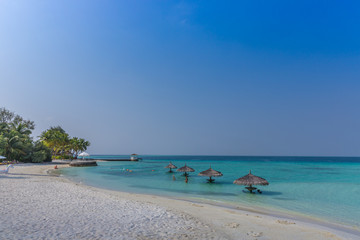 Fototapeta na wymiar Maldives, Feb 3rd 2018 - Beach umbrellas at the shallow blue water with some divers enjoying the tropical weather of Maldives