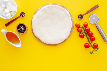 Make pizza concept. Pizza dough and ingredients for filling. Cherry tomatoes, olive oil, cheese mozzarella, spices near knife for pizza on yellow background top view mockup copy space