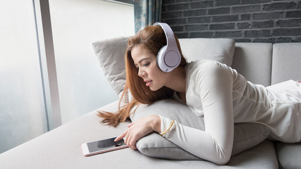 Asian woman relax on sofa bed, She listening to music from headphones.