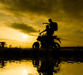 Silhouette Two brothers with a backpack riding a motorbike while the sun sets.