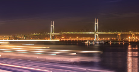 Fototapeta premium Panorama of Yokohama Bay Bridge from Ōsanbashi Pier with boats speed lights in the Minato Mirai district of Yokohama with boats under the night sky.