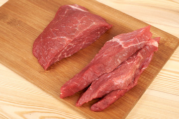 Raw beef piece and slices on wooden cutting board