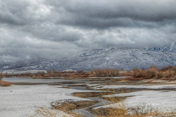 meandering stream flowing into lake in winter with snow and clouds