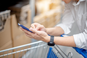 Young Asian man standing with cart checking the shopping list in warehouse wholesale, shopping warehousing concept