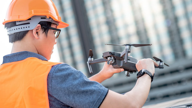 Young Asian engineer holding drone at construction site. Using unmanned aerial vehicle (UAV) for land and building site survey in civil engineering project.