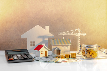 Real estate or property development. Construction business investment concept. Home mortgage loan rate. Coin stack on international banknotes with calculator, house and crane models on the table.
