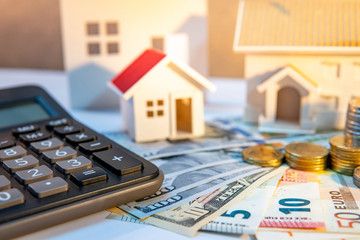 Real estate development or property investment concept. Home mortgage loan rate. Coin stack on international banknotes with house models and calculator on the table.