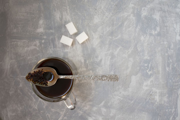 Black coffee cup with wighte sugar on black concrete background. Business work desktop with coffee. Coffee break concept with copy space for text, top view