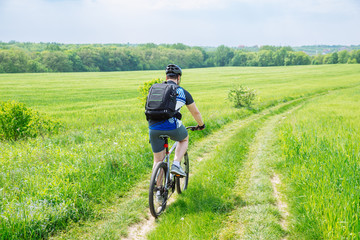 Fototapeta na wymiar man riding bicycle by trail in green barley field. copy space