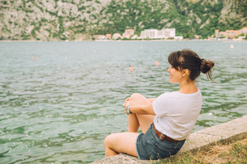 woman sitting at seaside looking at waves. mountains on background