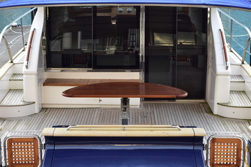 Wide stern deck with outdoor table and tinted glass door of large luxurious power catamaran.