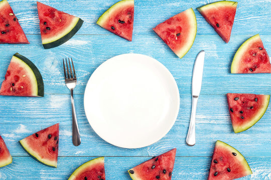 Summer table setting with cutlery and sliced watermelon on blue wooden table. Flat lay, top view, copy space.