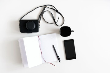 Blank notebook, pen, cup of coffee, retro camera, phone, on white office desk. Flat lay, top view, copy space 