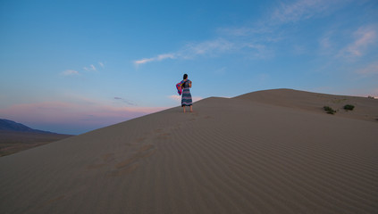 young girl in a dress on a sand dune at sunset