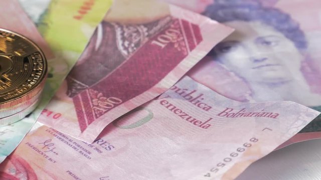 Physical metal Bitcoin currency over bolivar bills. Virtual internet money with Venezuelan banknotes. Digital coin cyberspace, cryptocurrency. BTC golden coin as symbol of electronic virtual money. 4K