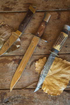Three hunting knives on old wooden background with autumn leaves,vertical picture