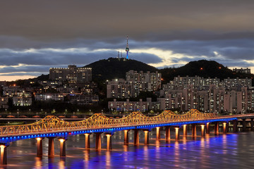 A bridge in front of Namsan Tower on a cloudy evening at sunset.