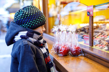 Little cute kid boy near sweet stand with sugared apples and chocolate fruits