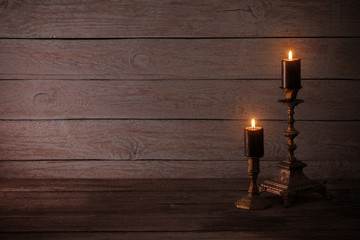 black burning candles in candlesticks on old wooden background
