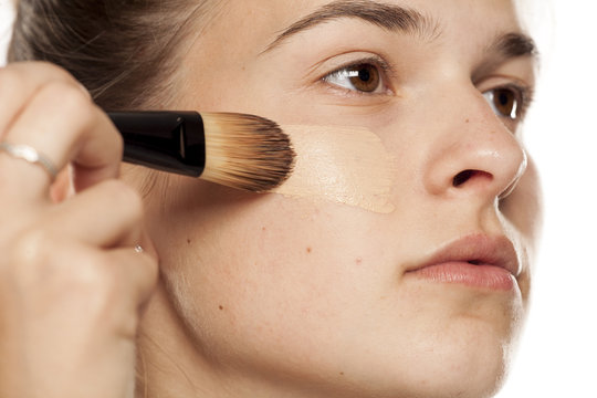 Fototapeta Young woman applying liquid foundation with brush on white background
