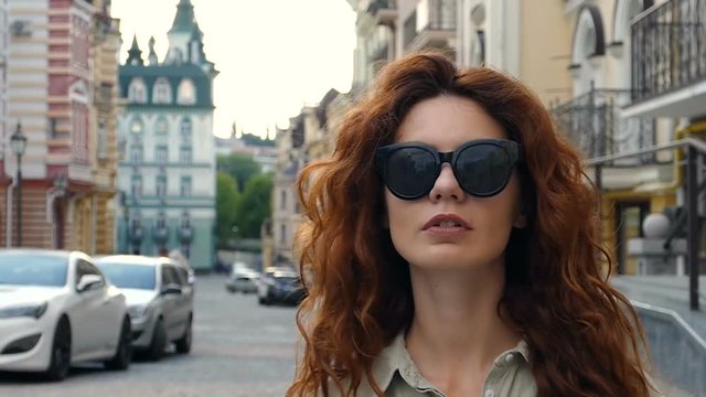 Attractive curly hair woman in black sunglasses walking at the street. Slow motion.