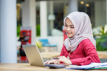 Young asian muslim woman working on laptop outdoor