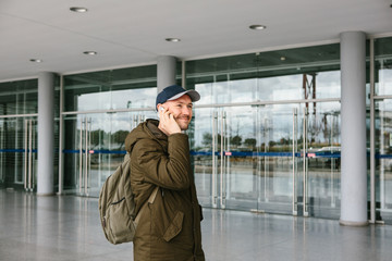 A young male tourist at the airport or near a shopping center or station calls a taxi or talks on a cell phone or communicates with friends using a mobile phone.